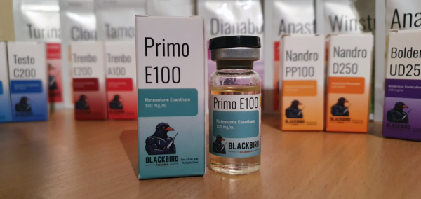 A product display of Primo E100 (Metenolone Enanthate 100 mg/ml) on a wooden tabletop.