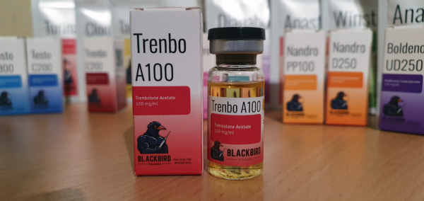 A product display of Trenbo A100 (Trenbolone Acetate 100 mg/ml) on a wooden tabletop.